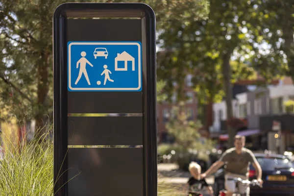 ALMELO, NETHERLANDS - Aug 02, 2020: Dutch traffic sign meaning you are entering a residential area with father and son out of focus in the background passing by. — Stock Image Almelo Netherlands Aug 2020 Dutch Traffic Sign Meaning You Entering Stock Picture