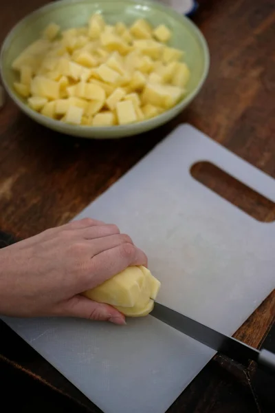 一个人在一块白色的切菜板上切土豆的垂直镜头 放在一张木制桌子上 — 图库照片
