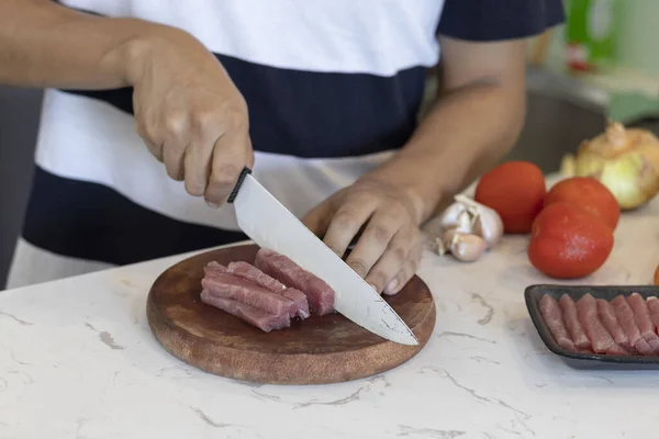 食材を入れたキッチンテーブルの上で牛肉をスライスする人のクローズアップショット — ストック写真