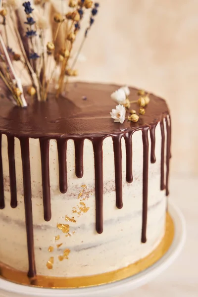 上にチョコレートドリップと花のあるバニラケーキの垂直ショット — ストック写真
