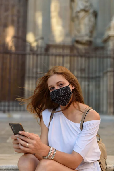 Μια Νεαρή Λευκή Γυναίκα Μια Μάσκα Κοιτάζοντας Μέσα Από Τηλέφωνό — Φωτογραφία Αρχείου