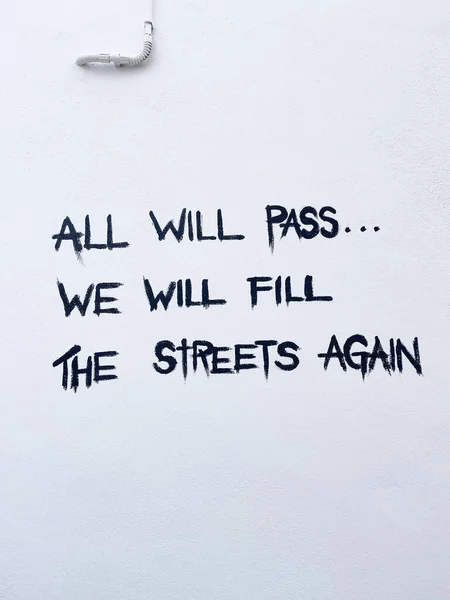 一道写着 一切都会过去 我们将再次填满街道 的垂直截图出现在一面白墙上 — 图库照片