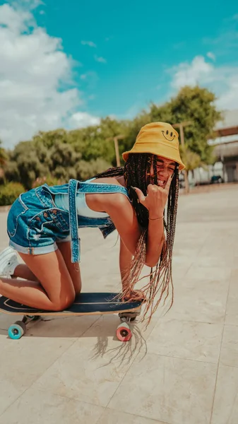 A female with dreadlocks in a bucket hat and with skateboard posing at camera