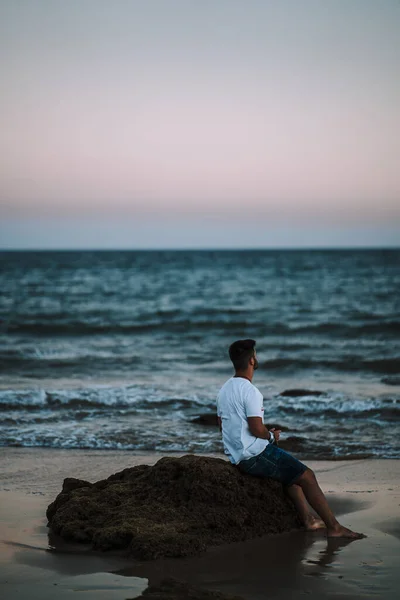 一个男人坐在海滩岩石上欣赏美丽的海景的令人惊奇的照片 — 图库照片