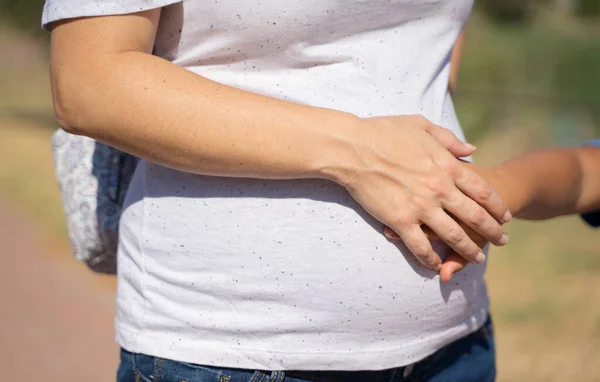 太陽の下で公園で妊婦の腹に触れる子供のクローズアップ — ストック写真