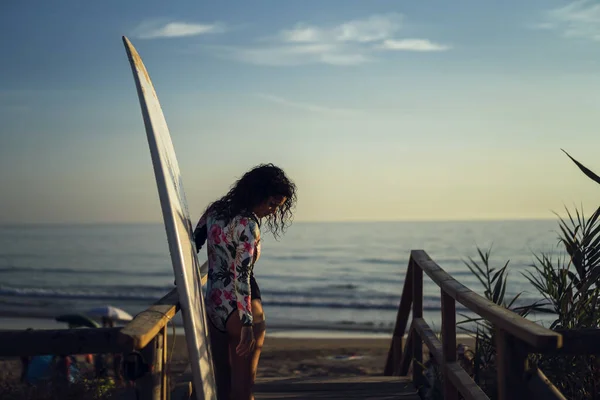 ビーチで木製のデッキに立ってサーフボードと水着の若い女性の浅い焦点 — ストック写真