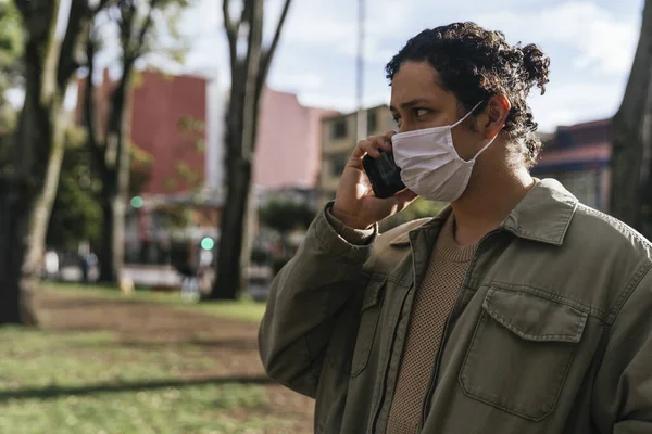 Een Jonge Spaanse Man Met Een Gezichtsmasker Aan Telefoon — Stockfoto
