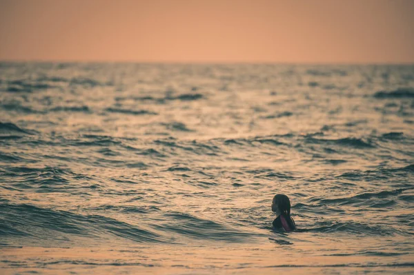 日没時に子供が水中で泳いでいるシルエット — ストック写真