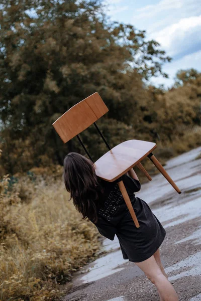 一个年轻女子白天拿着木椅的垂直镜头 — 图库照片