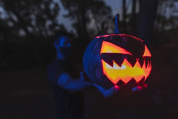 マスクを身に着けている若い男性の手の中に恐ろしい顔を持つハロウィンカボチャのクローズアップショット — ストック写真