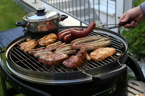 stock image A closeup of a person grilling sausages and steak on an outdoor grill in a garden at daytime