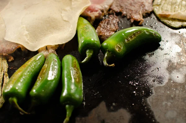 A closeup of meat grilling with jalapenos and welsh onions on the grill