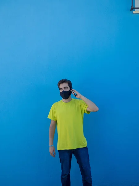 Mladý Evropan Žlutou Košilí Lékařskou Maskou Stojící Modré Stěny Mluvící — Stock fotografie