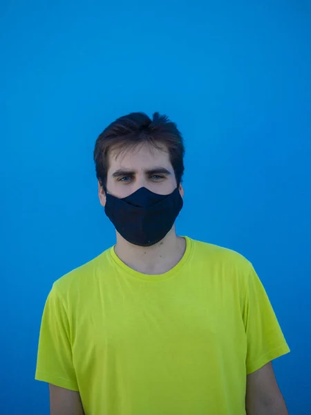黄色のシャツと青い壁に立っている医療用マスクを持つ若いヨーロッパの男性 Covid 19の後の新しい通常 — ストック写真
