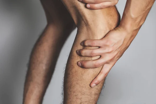 根据灰色背景健康护理理念拍摄的年轻成年男性膝部疼痛的特写镜头 — 图库照片