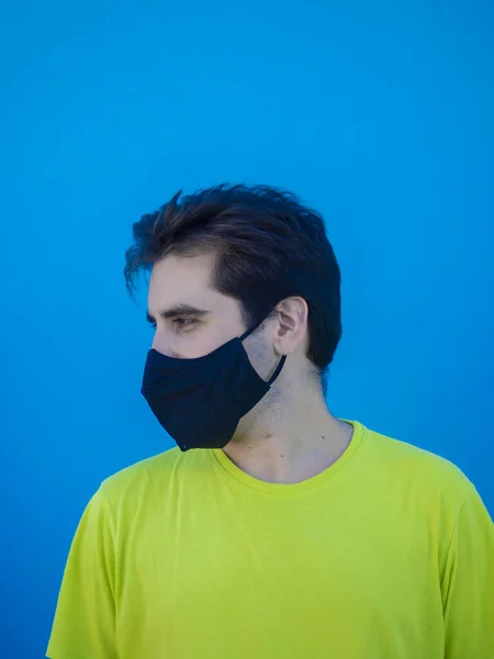 黄色のシャツと青い壁に立っている医療用マスクを持つ若いヨーロッパの男性 Covid 19の後の新しい通常 — ストック写真