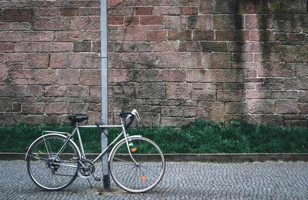 一辆旧自行车停在柱子旁边 后面有一堵石墙 — 图库照片