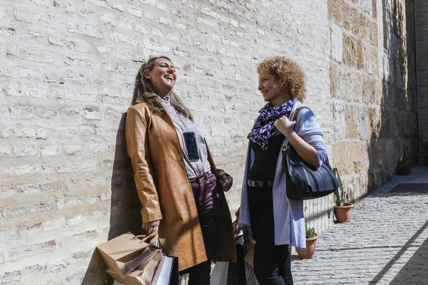 两个拿着购物袋在街上聊天的快乐的成年女子的照片 — 图库照片