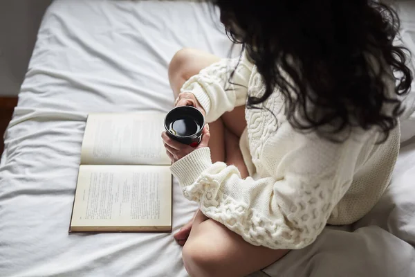 一个拉丁美洲的年轻女人喝咖啡 在床上看书 — 图库照片