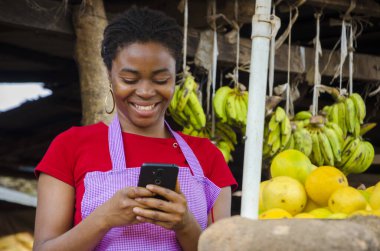 A young beautiful African market seller feeling happy about what she saw on her cellphone clipart