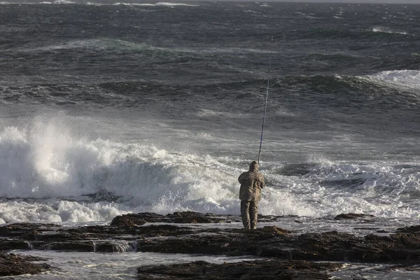 A back view of a person fishing in the sea with large waves