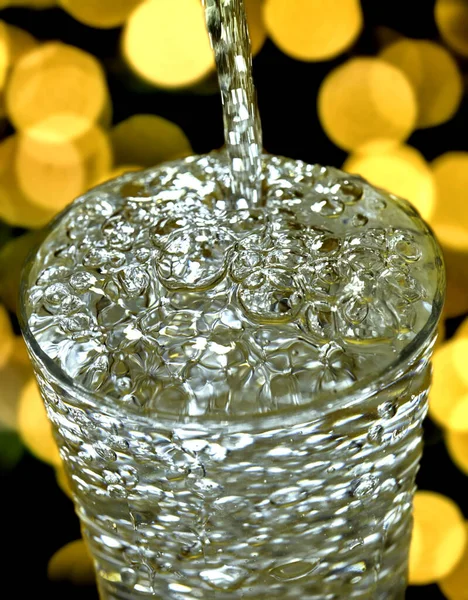 一杯垂直的特写水倒入玻璃杯中 玻璃杯的背景灯亮而明亮 — 图库照片