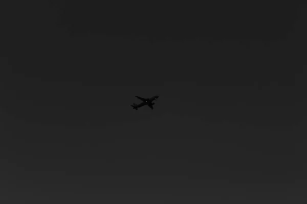 夕方には雲のない空を横断する飛行機の低角度のグレースケールショット — ストック写真