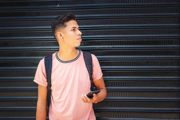 Joven Hispano Con Una Mochila Sosteniendo Teléfono Apoyado Contra Una —  Fotos de Stock