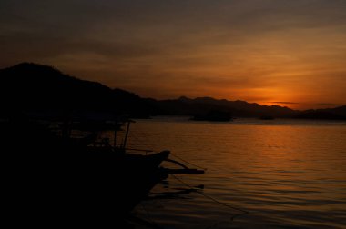 Coron, Palawan, Filipinler 'de dağ, deniz ve tekne siluetiyle gün batımı manzarası.