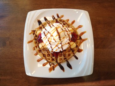 Muz, krema, dondurma, çilek reçeli ve waffle tatlı menüsünün üstüne de şurup.