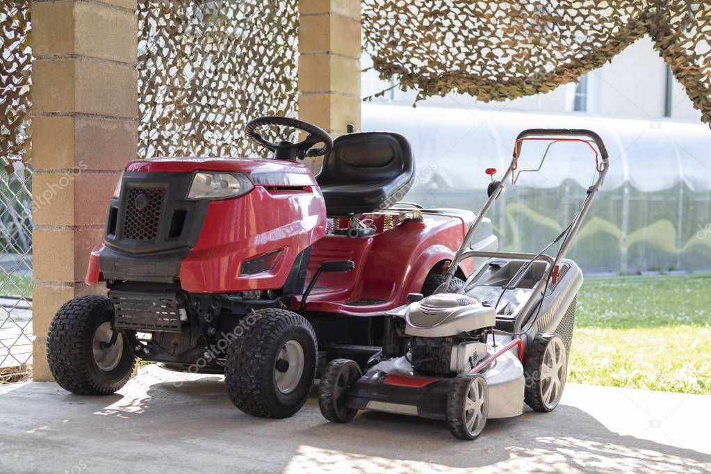 two models of lawnmower red and silver in the summer in the garden of the house