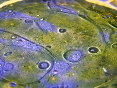 Mavi dokulu plaka soyut yağ lekeleri, damla, kabarcıklar su yüzeyinde. Alt tabakada ışık ışınlarının düşük açıda yağ desenleri gölgeler vardır. yakın kapatın. Sığ odak. doku arka planı.