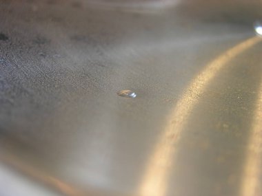 Metal sıcak kapak tavadan, yoğuşma ile kaplı. Bu gaz sobası üzerinde kaputtan lamba ışınları parlayan, pişirme buhar ile damlama olduğunu. metal üzerinde hemisperik bantlar vardır. Makro. Arka plan dokusu. Yumuşak odaklama.