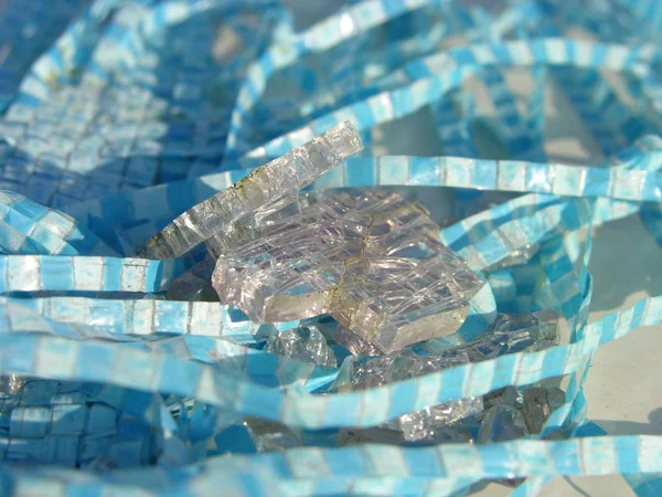 The squares are glass and squares are blue.  Contrasts - some hard, sharp, colorless, and other plastic, flexible and colored. Cubes of finely broken old tempered glass sparkle and shimmer in sun, reflecting the celestial color of tarpaulin. macro.