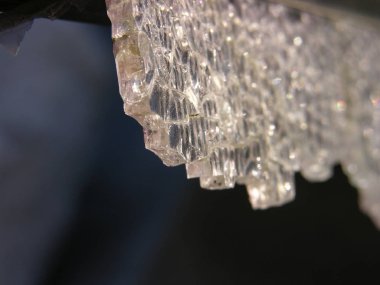 Karanlığın içinde asılı duran ağır bir kristal, düşmeye ve delmeye hazırdı. Renksiz, kaderin kurban silah kayıtsız (alegorik). kırık temperli cam yakın çekim. sığ odak.