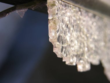 Karanlığın içinde asılı duran ağır bir kristal, düşmeye ve delmeye hazırdı. Renksiz, kaderin kurban silah kayıtsız (alegorik). kırık temperli cam yakın çekim. sığ odak.