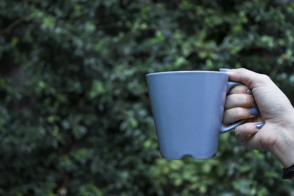 Mockup of female hand holding a coffee cup on natural garden — Stock Photo, Image