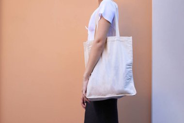 Boş beyaz alışveriş bezi kumaş çantası, elinde maket tutan kadın üzerinde ve izole edilmiş renk arkaplanı şablonu.