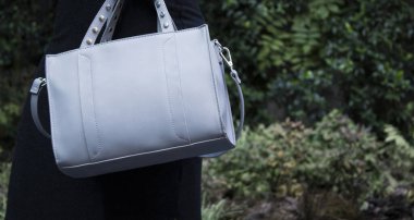 Gri deri kumaşlı kadın çantası, doğal arka planda moda modeli.