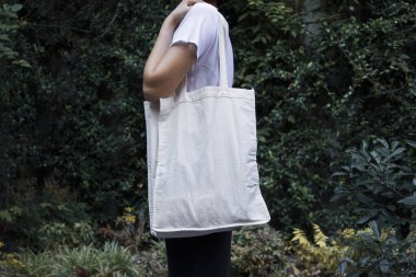 Boş beyaz alışveriş tuvali. Kumaş çanta. Elinde maket tutan ve doğal arka plan kalıbı olan kadın üzerinde.