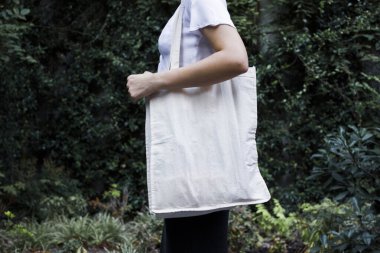 Boş beyaz alışveriş tuvali. Kumaş çanta. Elinde maket tutan ve doğal arka plan kalıbı olan kadın üzerinde..