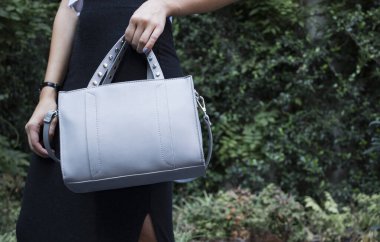 Gri deri kumaşlı kadın çantası, doğal arka planda moda modeli.