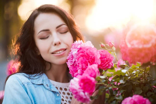 Smiling woman 24-25 year old smelling roses outdoors closeup. Summer season. 20s.