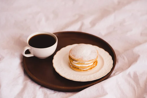 Fresh morning cup of coffee with pancakes on wooden tray in bed closeup. Good morning. Selective focus.