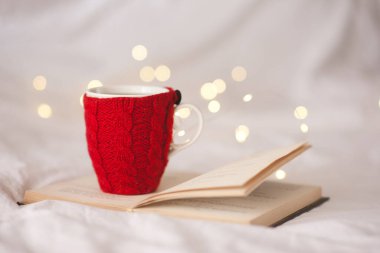 Örülmüş bir fincan çay arka planda parlayan ışıklarda açık bir kitabın üzerinde duruyor. Kış tatili. Xmas. 