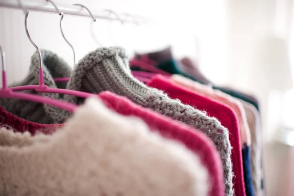 Colorful knitted clothes hang on hangers in shop closeup. Winter season. Selective focus.