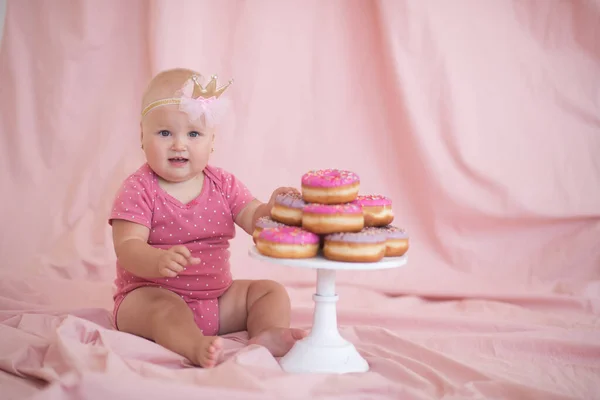 一岁的女婴穿着紧身衣和小皇冠帽带 在粉红纺织品背景特写的房间里吃着美味美味的食物 胆大妄为第一个生日聚会 — 图库照片