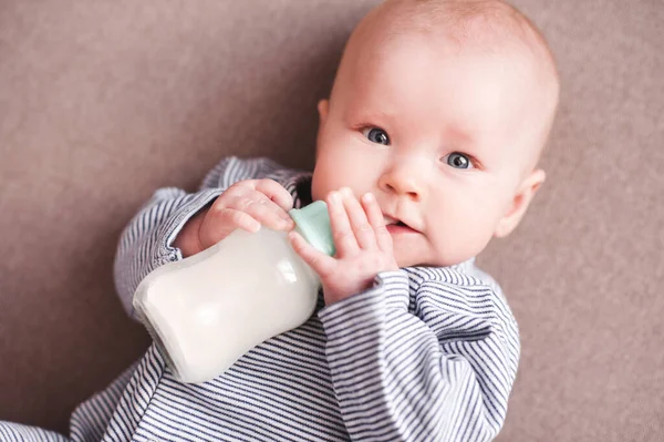 新生儿抱着奶瓶躺在床上喝水 看着摄像机 健康营养 — 图库照片
