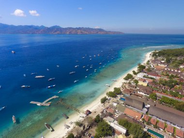 Endonezya 21 Haziran 2020: Beyaz kumlu plajlı tropikal ada ve mavi şeffaf su ve mercan resifleri. Hava saldırısı, sürat tekneleri, uzun kuyruklu botlar, Gili Trawangan Adası Endonezya