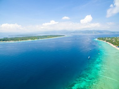 Endonezya 21 Haziran 2020: Beyaz kumlu plajlı tropikal ada ve mavi şeffaf su ve mercan resifleri. Hava saldırısı, sürat tekneleri, uzun kuyruklu botlar, Gili Trawangan Adası Endonezya